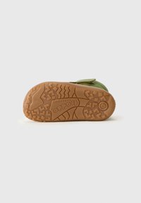 Zapato de ante verde con una suela de goma que presenta un patrón de textura en la suela y una correa de velcro. Logo visible en la suela.