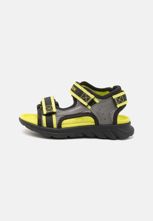 Black and grey sandal with yellow accents, featuring adjustable straps, a textured footbed, and a flexible, rugged sole. Water-friendly design.