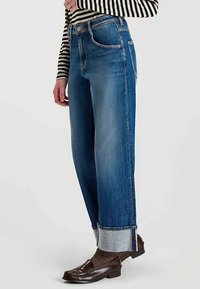 Jean denim bleu taille haute, coupe décontractée avec revers retroussés. Comprend cinq poches et une fermeture classique avec bouton et fermeture éclair.