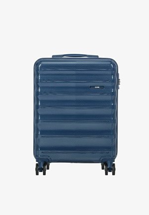 Niebieska teksturowana walizka z twardą skorupą, wyposażona w cztery czarne obrotowe kółka i górny uchwyt do przenoszenia, stojąca pionowo na białym tle.