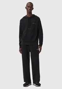 Zwarte hoodie met voorzak en trekkoord, gecombineerd met bijpassende zwarte joggingbroek. Voorzien van subtiel logodetail en gestructureerde stof.