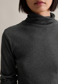Grå ribbede turtlenecksweater, med en tætsiddende pasform, lange ærmer og en tekstureret overflade. Halsudskæringen er foldet i en blød, fremtrædende rul.