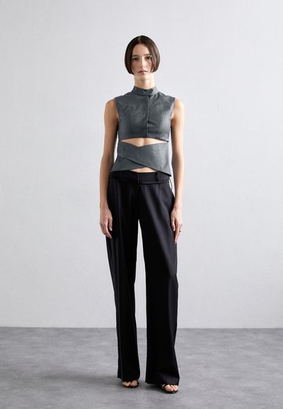 Gray sleeveless top with a high neckline and cut-out midsection, paired with black, wide-legged trousers. Smooth texture, modern design.