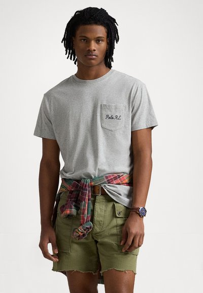 Szary bawełniany t-shirt z kieszonką i haftem "Polo R.L."; w kratę flanela związana w talii; oliwkowe szorty z postrzępionym dołem.