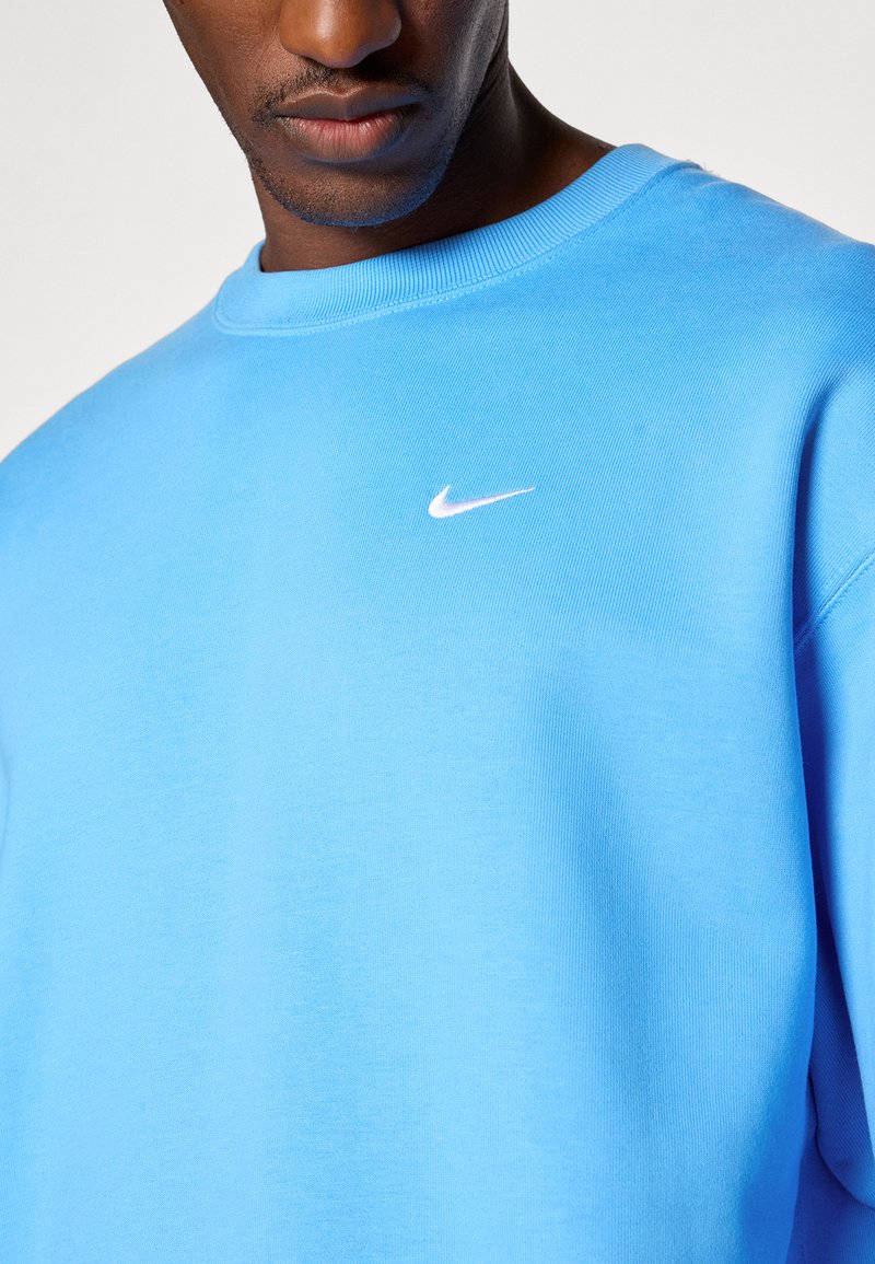 Jasnoniebieski bawełniany sweatshirt z prążkowanym dekoltem, z białym logo Nike na piersi. Gładka tekstura, klasyczny fason z okrągłym dekoltem.