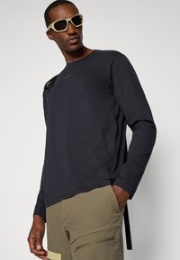 Zwart langarmshirt van lichtgewicht stof, met een ronde hals, zijnaad en een subtiele logo op de borst.