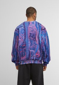 Übergrößer Pullover-Sweatshirt mit einem bunten abstrakten Muster in Blau- und Rosatönen, versehen mit gerippten Bündchen und Saum.