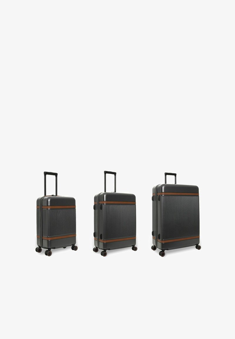 Trois valises rigides noires avec des accents marron, chacune équipée d'une poignée extensible et de quatre roues pivotantes, disposées de la plus petite à la plus grande.