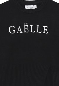 Maglione nero a maglia con orlo e polsini a coste, che mostra in modo prominente il logo "GAËLLE" in lettere bianche sul davanti.