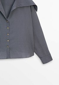 Chemise bleu marine à manches longues avec fines rayures verticales blanches, boutons dorés sur le devant et large col.