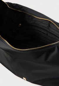 Interiorul sacului negru din nailon cu fermoar auriu, prezentând o textură fină și o căptușeală marcată cu modelul „TOMMY HILFIGER”.