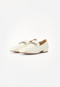 Elfenbenfärgade patentläder loafers med platt klack, spetsig tå och en dekorativ rad av strass framtill.