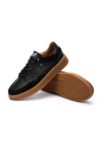 Zapatilla negra hecha de cuero y ante con un diseño perforado, suela de goma color marrón y detalles de logotipo en la lengüeta y el lateral.