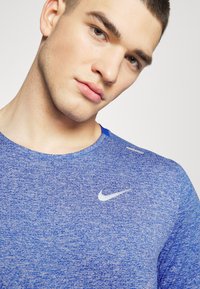 Maglietta atletica blu a maniche corte con tessuto a maglia testurizzata. Presenta un logo Nike riflettente e discreto sul petto e un collo arrotondato.