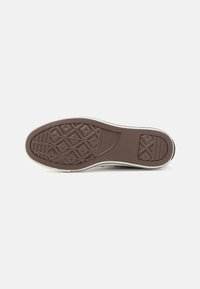 Rubber shoe sole in brown with textured patterns, including a diamond grip design. Edges are curved with a slight white border.