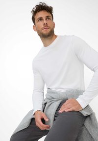 Hvid langærmet t-shirt lavet af bomuld, med en rund halsudskæring. Grå strikket trøje rundt om taljen, med grå bukser.