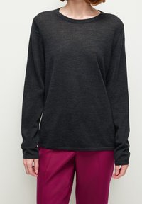 Pitkähihaisen tummanharmaan villapaidan kevyt materiaali, jossa on pyöreä kaula-aukko ja rento istuvuus. Yhdistetty vaaleanpunaisten housujen kanssa.