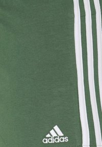 Pantalones cortos deportivos verdes hechos de una mezcla de algodón, con tres rayas verticales blancas en el lateral y un pequeño logo de Adidas en blanco.