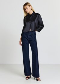 Schwarze, aus Satin gefertigte, kurz geschnittene Bluse mit Kragen und Knopfverschluss, kombiniert mit hoch taillierten, marineblauen Jeans mit weitem Bein und dezentem Schimmer.