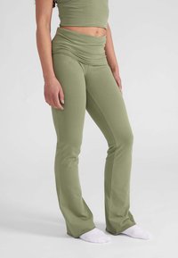 Olijfgroene rekbare flared broek met een hoge, geraffineerde tailleband en een gladde textuur, gecombineerd met witte enkelkousen.