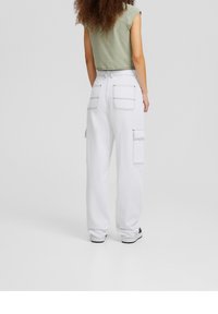 Pantalones cargo blancos con bolsillos laterales, con costuras en contraste y un ajuste relajado. Combinados con una blusa sin mangas de color verde claro.