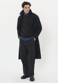 Jūras spēku mētelis, tumšs džemperis, zila džinsu krekls, melnas plisētas bikses un masīvas melnas kurpes ar bieziem šņorēm. Vienkāršs, mūsdienīgs dizains.