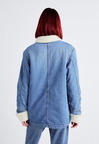 Leren denim jack in lichtblauw met een witte nep-shearling kraag en manchetten. Heeft een ontspannen pasvorm en zichtbare stiksels langs de naden.