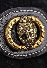 Matière en cuir texturé noir avec une boucle ovale dorée ornée d'un design décoratif composé de segments superposés et d'accents noirs.