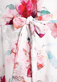 Floral dress with a soft, sheer fabric featuring a white background and pink, red, and green flower patterns. Waist tied with a fabric bow.