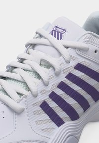 Λευκό παπούτσι K-Swiss με μοβ ρίγες στο πλάι, λευκά κορδόνια και λεπτομέρειες από δίχτυ στη γλώσσα και τις πλευρές.