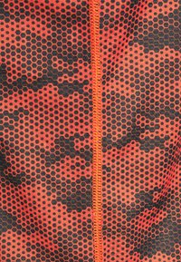 Röd och svart hexagonal mönstrad tyg med en slät textur, med en orange central söm och stygn.