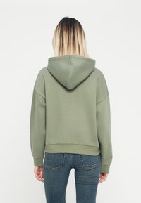 Olijfgroene hoodie met een achterzak en een aangesloten zoom. De capuchon heeft een subtiele naad en de stof lijkt zacht met een gladde textuur.