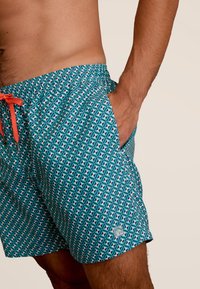 Zwemshorts met een geometrisch patroon in turquoise en zwart. Beschikt over een elastische tailleband, oranje trekkoord en zijzakken.