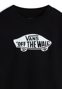 Černé bavlněné tričko se velkým bílým potiskem loga skateboardu se textem "Vans 'OFF THE WALL'" v tučném písmu.
