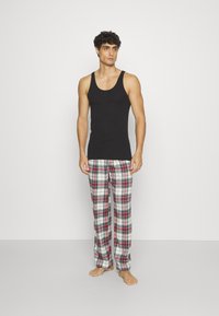 Un débardeur noir et un pantalon de pyjama à carreaux en blanc, rouge et bleu. Le pantalon présente une taille élastique et une coupe droite.
