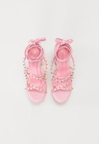 Rosa sandaler med en glatt overflate, med flere stropper, gullnagler og en sløyfedetalj ved ankelen. Flatt hældesign.