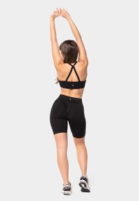 Must värvitud spordibrasi ristatud seljapatjadega, koos mustade rattasõidupükstega, sile kangas, lõikekujundus, kantud jooksujalatsitega.