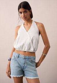Bela halter majica s nabranim rubom uparen s svijetloplavim traper kratkim hlačama s uskraćenim rubovima i suptilnim ukrasima.