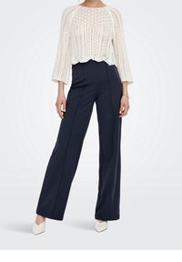 Top corto lavorato a maglia bianco con orlo a scallop e maniche a campana, abbinato a pantaloni navy a vita alta e a palazzo e tacchi a punta bianchi.