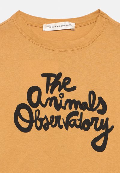 Жълта риза с черен текст с надпис "The Animals Observatory" в стилизиран, ръкописен шрифт на гърдите.
