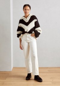 Suéter de chevron en blanco y negro con capucha, combinado con jeans rectos blancos y botines de plataforma negros.