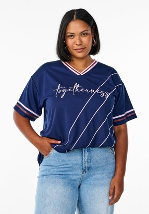 Marineblaue Sport-T-Shirt mit kurzen Ärmeln, V-Ausschnitt, pinken Akzenten und weißem Text "Gemeinsamkeit" sowie diagonalen Streifen. Jeans in Denim.