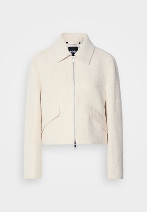 Cropped jacket in off-white textured fabric, featuring a stand collar and side pockets, with a front zipper closure and minimal hardware.