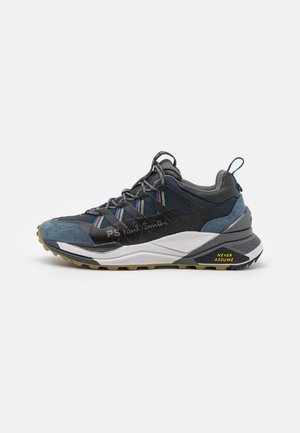 Baskets gris foncé et bleues avec des rayures multicolores, logo PS Paul Smith, semelle épaisse, et texte jaune "Never Assume" sur le talon.