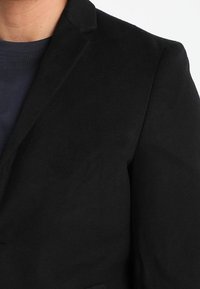 Zwarte blazer met een gladde textuur, enkele knoopsluiting en ingesneden revers. Bevat subtiele stikseldetails en een slim fit ontwerp.