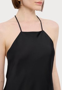 Black silk halter top featuring thin straps, a smooth texture, and an A-line silhouette. Minimalist design with no visible patterns or hardware.