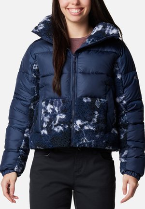 Giacca puffer blu navy con una parte anteriore e maniche soffici e testurizzate. Presenta una chiusura con zip e due tasche frontali, con una silhouette aderente.