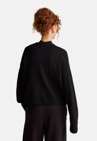 Schwarzer gestrickter Pullover mit geripptem Saum und Bündchen, mit Rundhalsausschnitt und lockerer Passform. Strukturierter Stoff, lange Ärmel, verkürzte Länge.