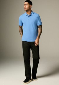 Světle modré polo tričko s krátkými rukávy a límečkem, spárované s černými kalhotami a černými teniskami s bílou podrážkou.