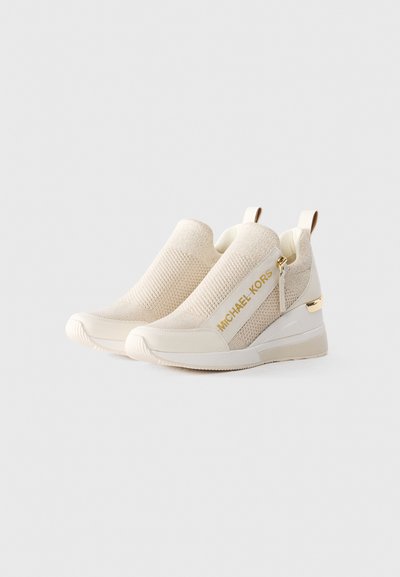 Baskets slip-on beiges avec texture en tricot, fermeture éclair dorée et détail de logo, col élastique et semelle en caoutchouc blanche à talon compensé.